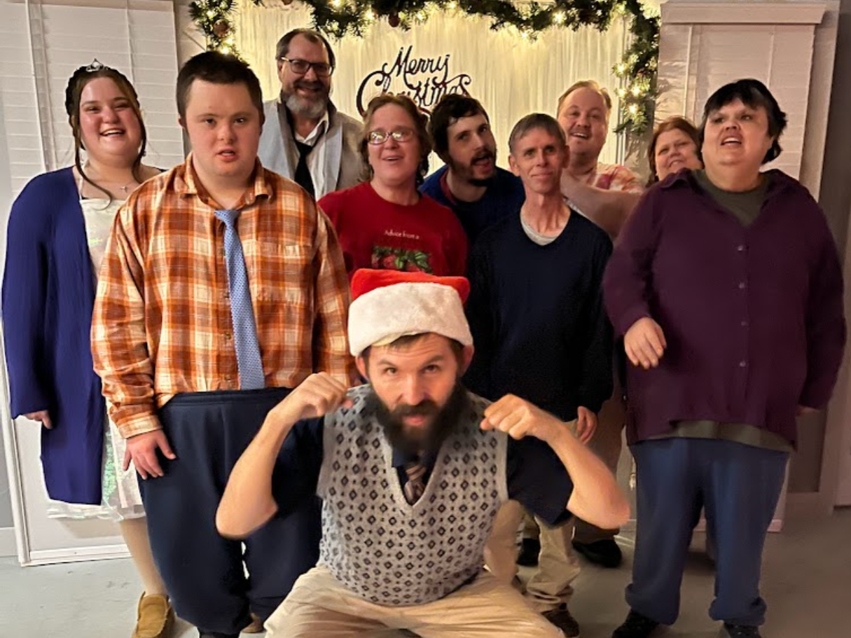 A group of individuals smiling and posing together in front of a beautifully decorated Christmas tree.