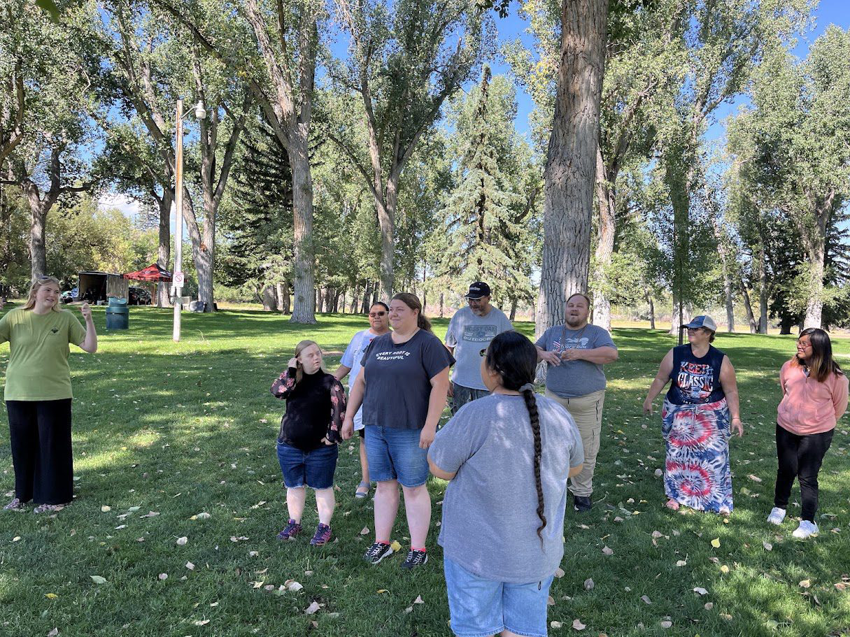 A group of people standing in a sunny park with trees and grass.