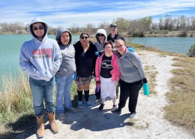 A diverse group of individuals stands on a dirt path beside a serene lake