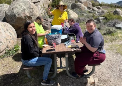 A group of individuals enjoying a meal together at a picnic table surrounded by majestic mountains